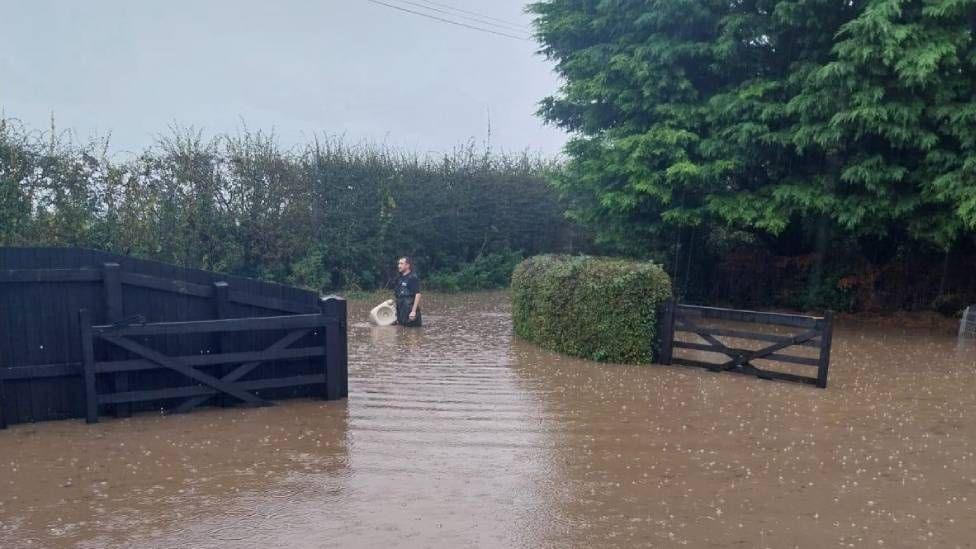 A man wading through waist-high water near to a fence 