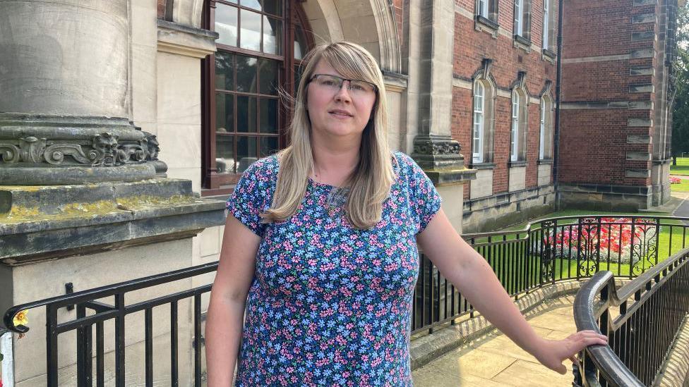 Claire Calvert in a top with flowers on it stood on the steps at the front of County Hall in Northallerton