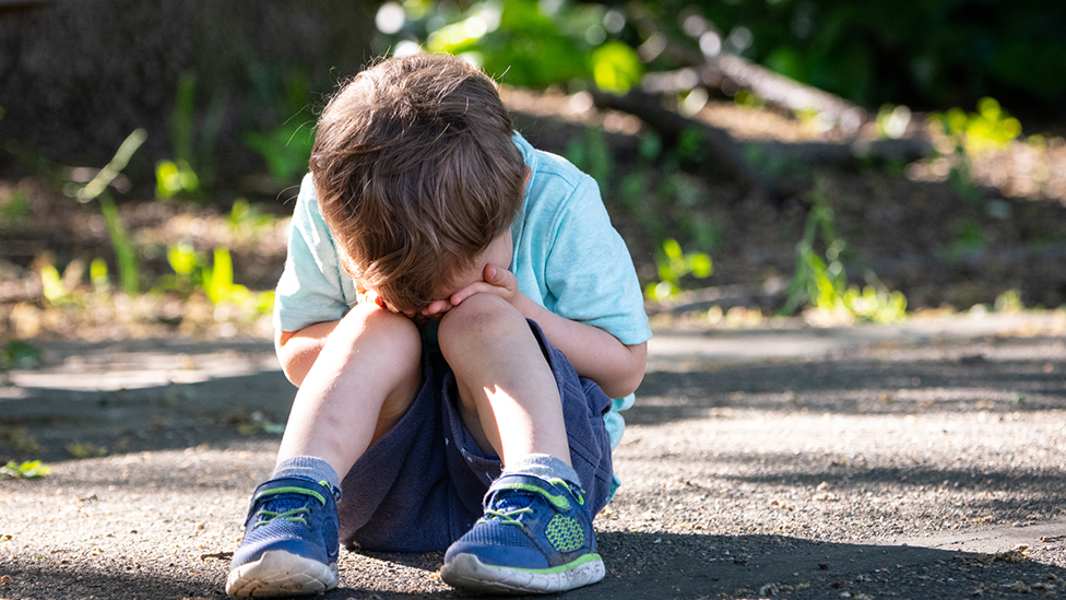 Generic image of young child sitting on pavement with head in hands crying