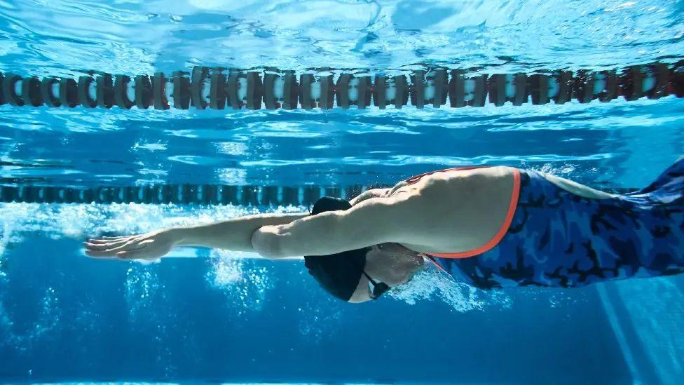 Generic image of a female swimmer underwater in a swimming poole with arms stretched ahead of her