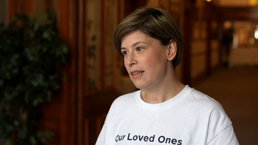 A young woman wearing a white t-shirt bearing the words 'Our Loved Ones' 