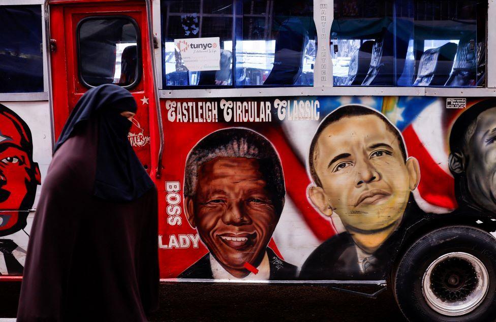 A woman wearing an abaya and niqab walks past a bus with artwork depicting late South African President Nelson Mandela and former US President Barack Obama, whose later father was Kenyan. 