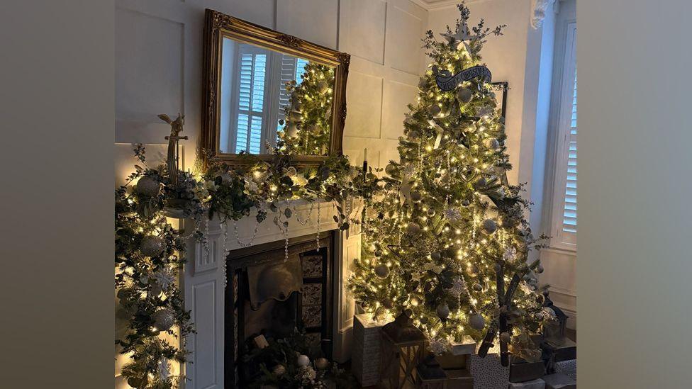 A Christmas tree with white lights and a fireplace with a Christmas garland and white lights