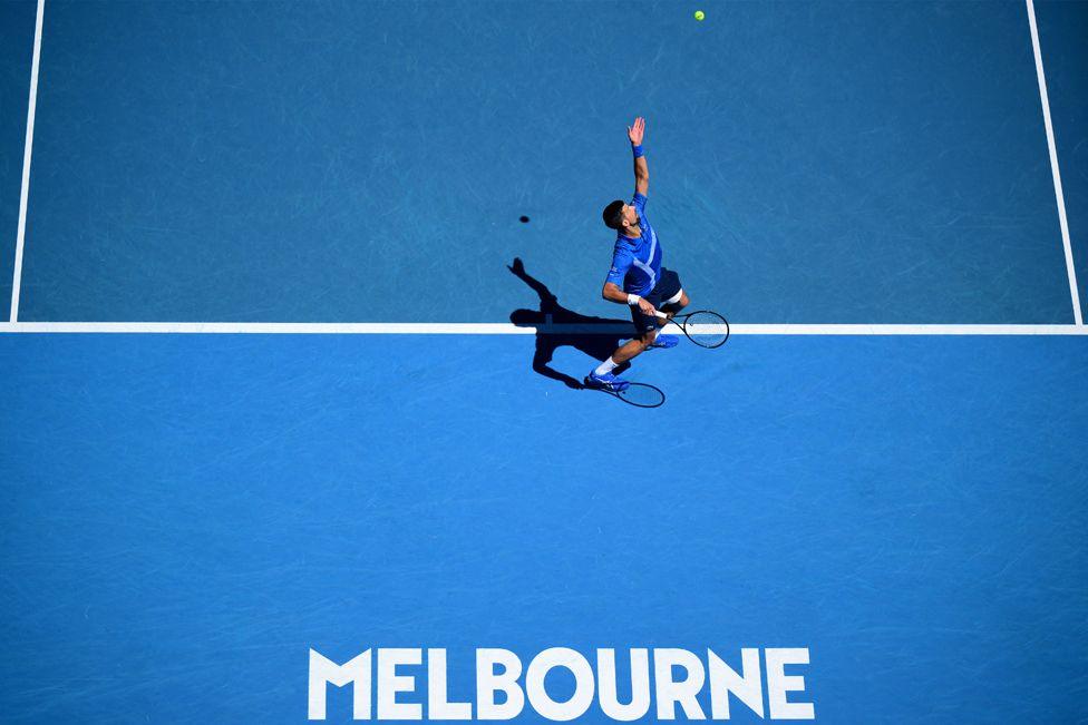 Serbia's Novak Djokovic serves against Germany's Alexander Zverev during their men's singles semi-final match on day 13 of the Australian Open tennis tournament in Melbourne on January 24, 2025. The court is blue and has the word Melbourne printed in white capital letters at the bottom of the frame.