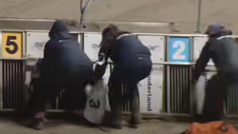 People leaning over the racing traps as they try to help the dogs.