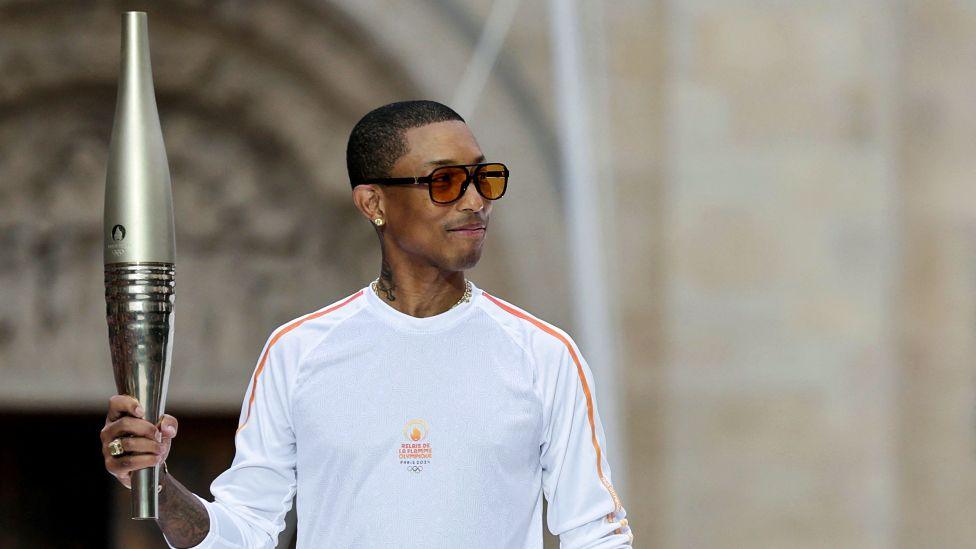 US rapper, artist and designer Pharrell Williams holds the Olympic torch as part of the 2024 Paris Olympic Games Torch Relay, on the day of the opening ceremony.