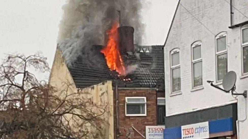 Phone image of the fire showing flames and thick smoke bursting through the slate tiles on the roof of a terrace house