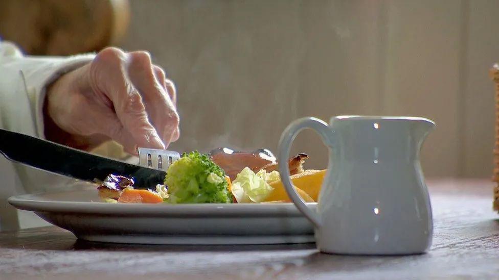 A close-up of a plate of food while somebody is eating. A white milk jug is placed on the table next to the plate.