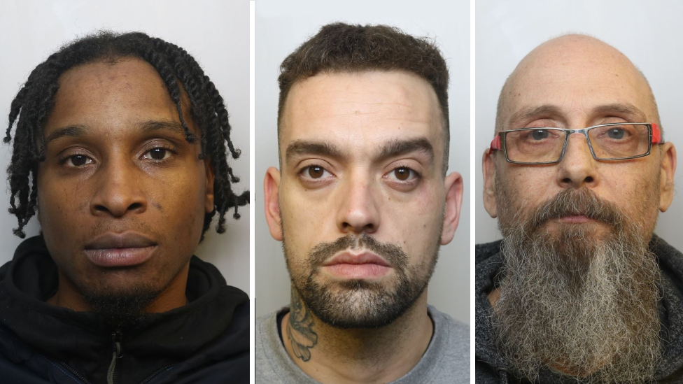 A side by side of three police mugshots. On the left is Smith wearing a black zip up jumper. He has his hair twisted into braids and is clean shaven with brown eyes. In the middle is Gregory, wearing a grey t-shirt. He has a dark trimmed beard, brown eyes and a neck tattoo on his right side. On the right is Adrian Williams, who is bald with a long grey and brown curly beard, wearing thin metal framed rectangular glasses with red arms on them.