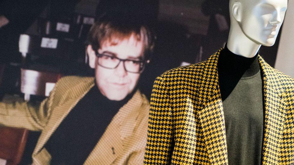 A yellow blazer worn by Sir Elton John, shown as part of the exhibition and featured next to a picture of the singer wearing it