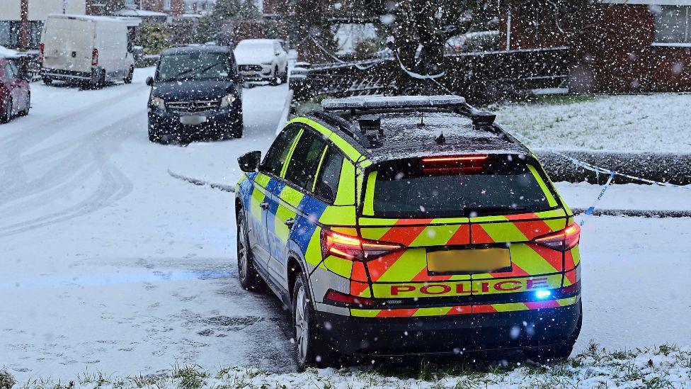 Police cordon and car outside a residential area. Snow is on the ground.