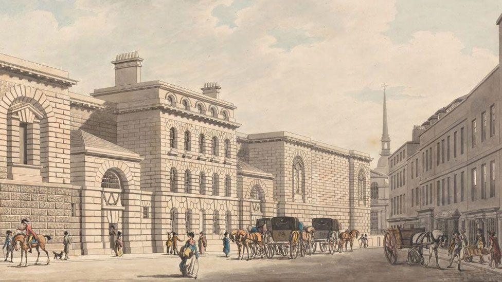 A sepia drawing of Newgate Prison in the late 18th Century, showing the prison building on the left. It rises four stories and is made of brick. On the right is a four storey terrace. And in front are carriages with horses, a cart pulled by a horse and men and women walking around