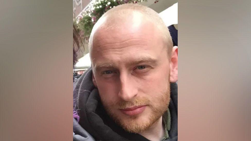 An image of Lee Star, whose face is close to the camera for a selfie. He has a light, close-cropped beard and a shaved head