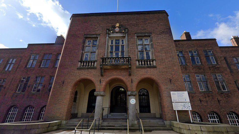 A street view image of the front of Dudley town hall. It is a brick building with arches at the front, a crest above the top window and a flagpole on the roof.