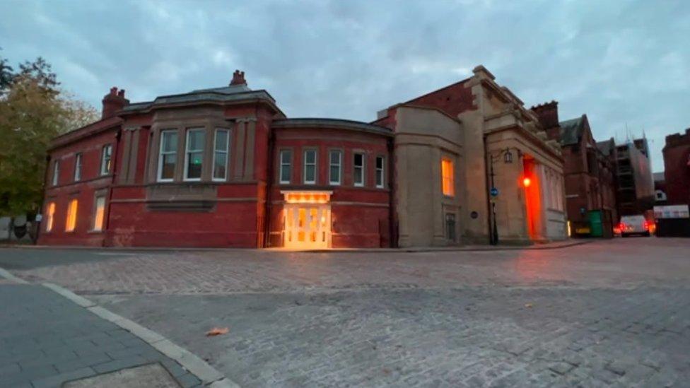 Drapers' Hall in Coventry at dusk. There are lights on the outside of the building, and lights can be seen through some of the windows.