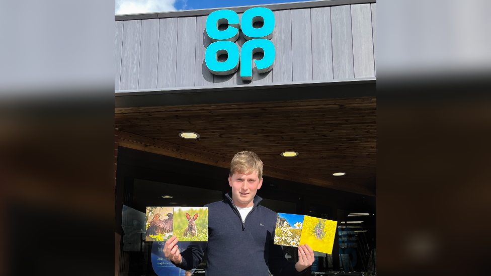 Ben outside a Co-op store holding his cards