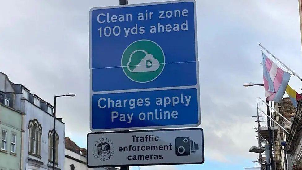 A blue road sign which says 'Clean air zone 100 yds ahead charges apply pay online'