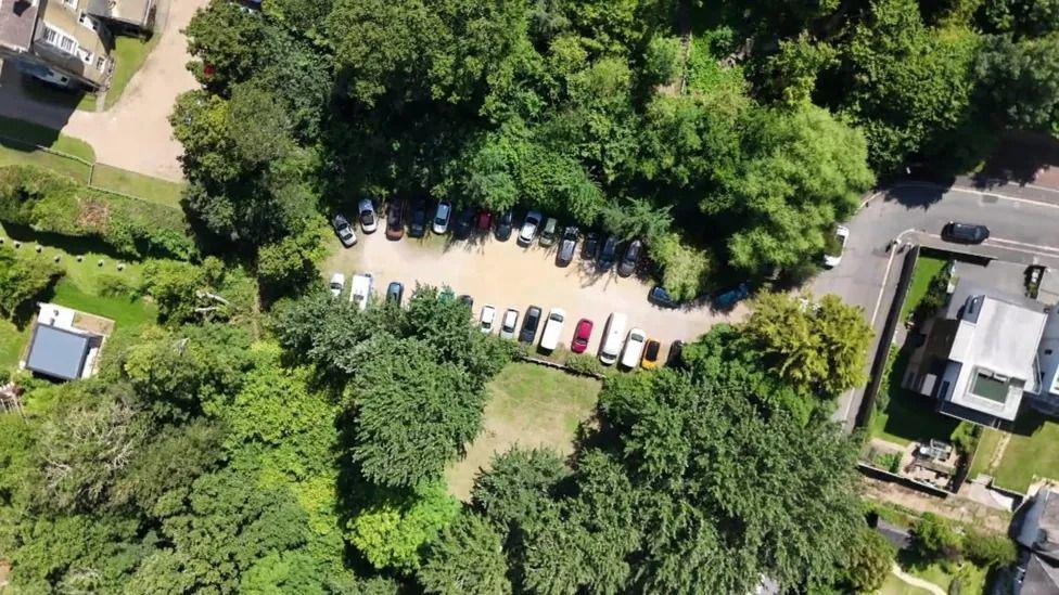 A drone shot of Mornington Road car park with trees encircling the car park where cars can be seen.