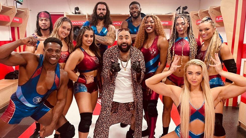 Chabuddy G actor Asim Chaudhry surrounded by the cast of Gladiators