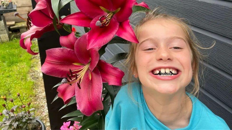 Scarlett Rossborough smiling beside large pink lily