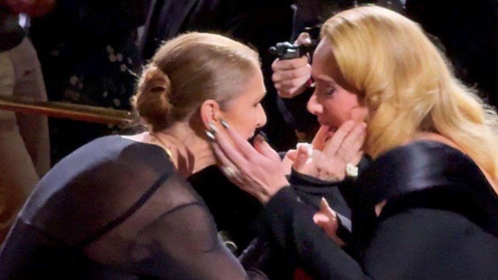 Adele and Celine Dion holding each other's faces in their hands