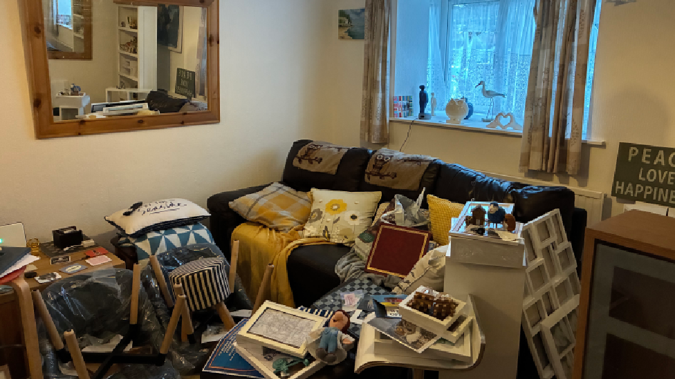 Pentwr o bethau amrywiol ar, ac o amgylch, soffa ledr ddu yn yr ystafell fyw