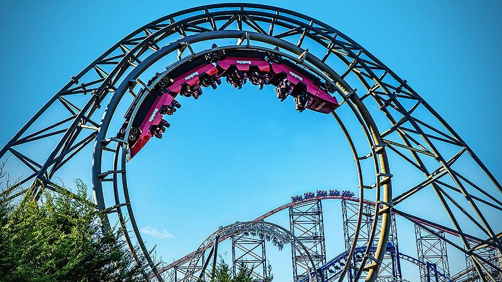 Blackpool Pleasure Beach rollercoasters including Revolution in the foreground, a huge circle of track with a pink carriage upside down at the top mid-ride