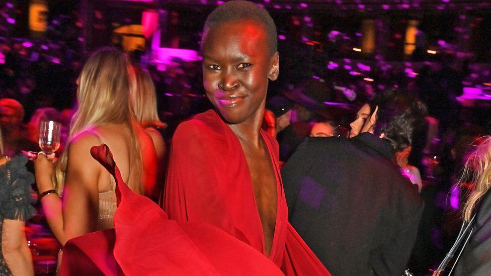 Alek Wek in a red dress smiles at the camera during The Fashion Awards 2024 after party presented by Pandora at Royal Albert Hall in London, the UK - December 2024