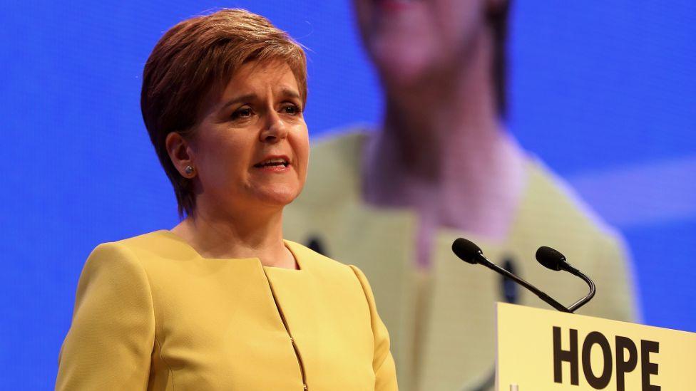 Nicola Sturgeon wearing a yellow suit standing on stage at the SNP conference 