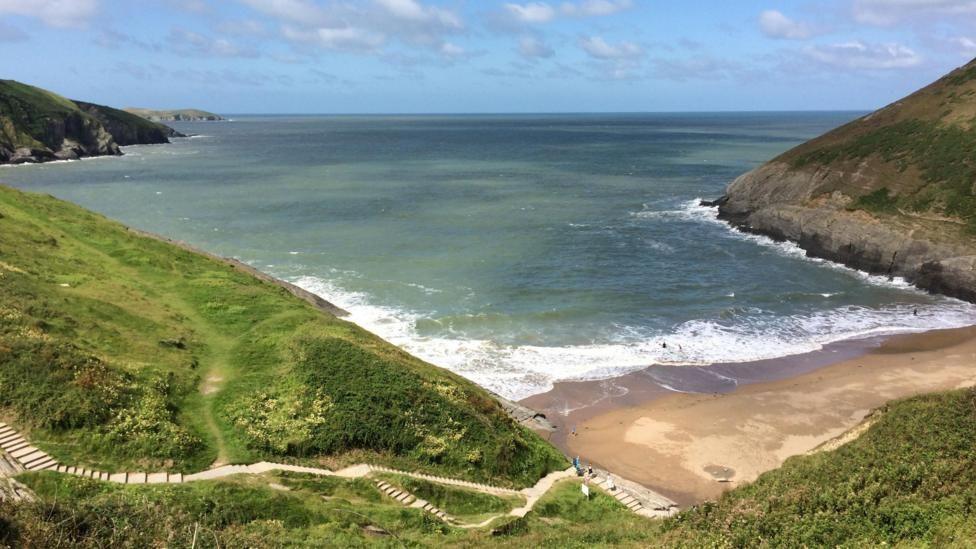 A view from a clifftop down onto a sandy beach with the tide quite far in and cliffs on either side.