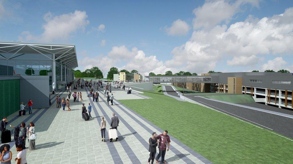 A computer generated image of what the expanded airport would look like. There is a multi-storey car park on the right and a glass tunnel that leads to the airport on the left. There is a large open paved area with a grass strip in the middle.