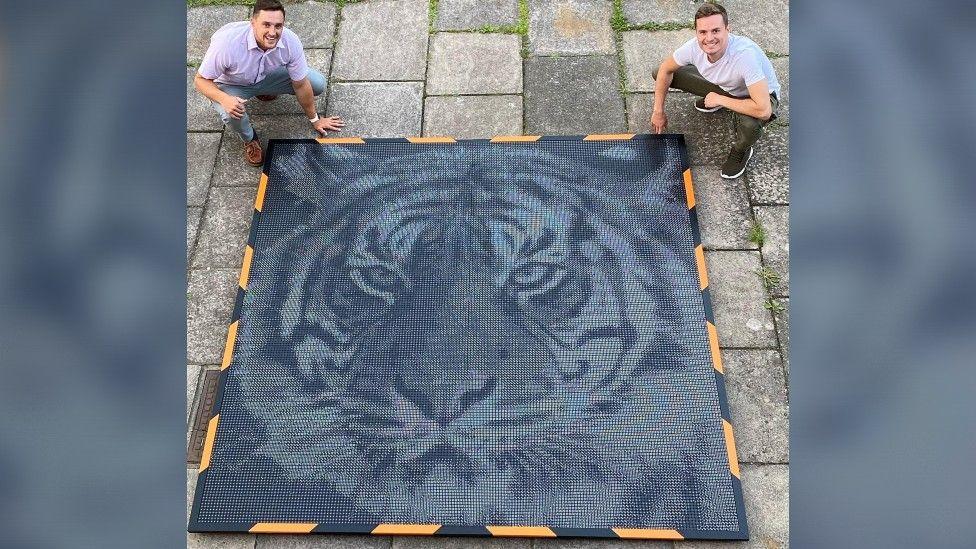 Image of Ross and Ben crouching next to large artwork of a tiger placed on the floor