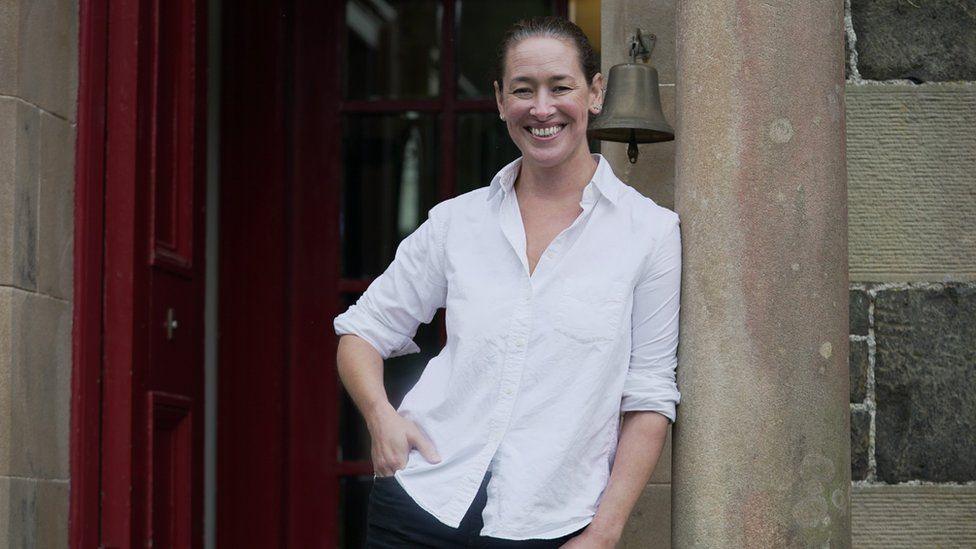 Fiona Chaimbeul na seasamh air beulaibh taigh