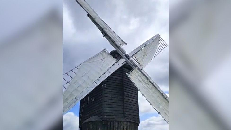 The windmill has a wooden frame which has been painted black. The rotating arms have been painted white and now have material wrapped around them to make them rotate in the wind.