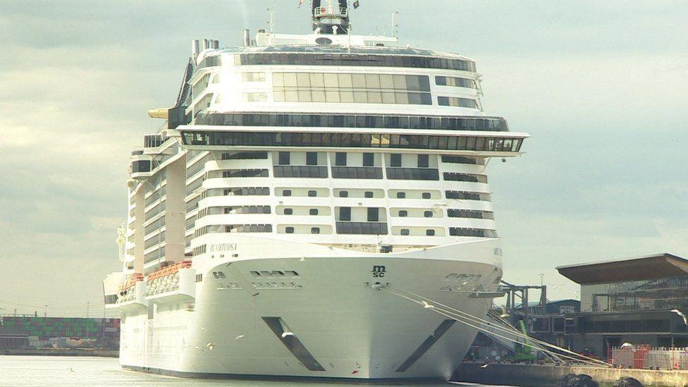White cruise ship berthed with ropes to its left side onto the docks.