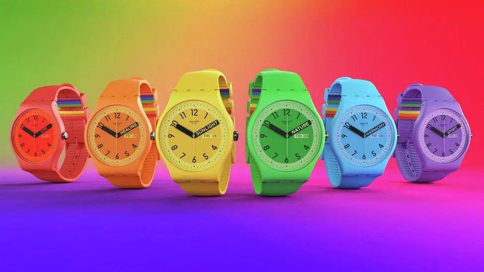 Six Swatch watches, each a bright colour. A rainbow pattern is on the strap