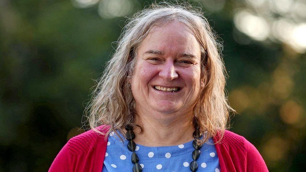 Head and shoulders shot of Roxanne Tickle smiling and looking at the camera while standing outside with greenery in the background, supplied by her lawyers