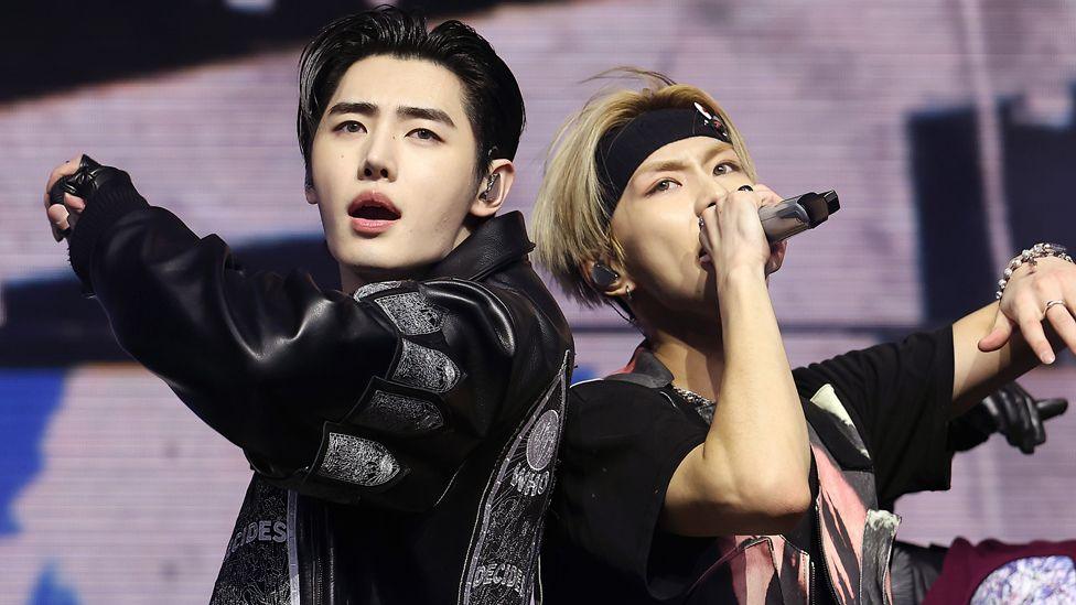 Sunghoon, with black hair and wearing a black leather jacket, and Jungwon, with blond hair, a black headband and a black T-shirt, of ENHYPEN perform at Sahara Tent during the 2025 Coachella Valley Music and Arts Festival
