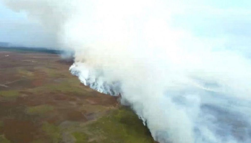 Thick smoke billowing from fields as a fire burns.