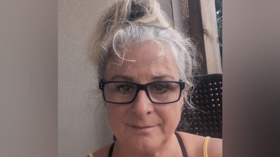 A woman with white grey hair and black glasses taking a selfie