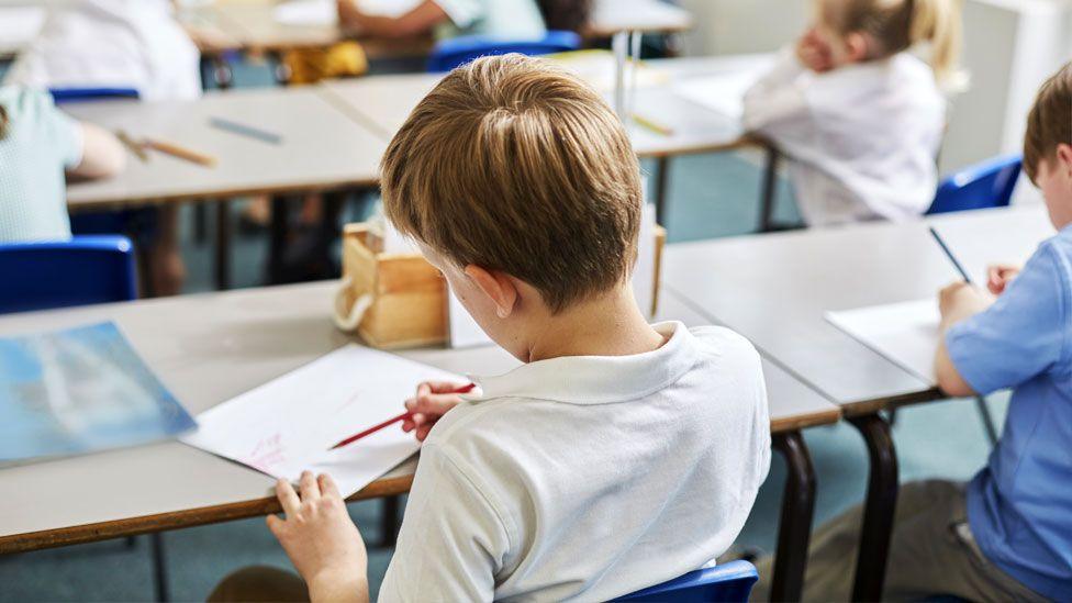 Schoolchildren in classroom holding pencils and writing in exercise books 