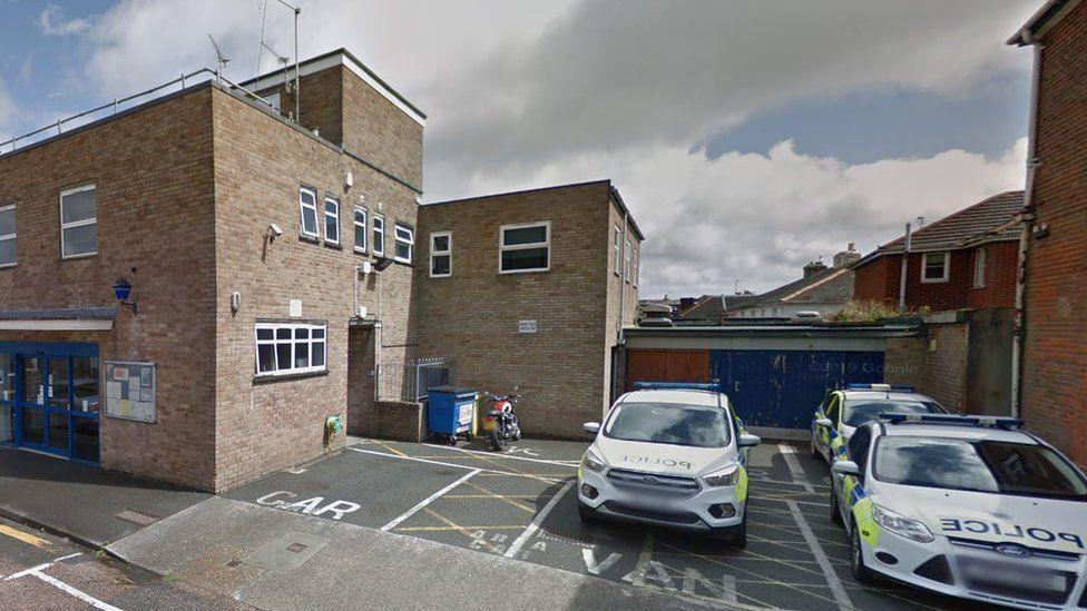 Three police cars parked on forecourt with beige  brickwork police building to left with white window and blue doors