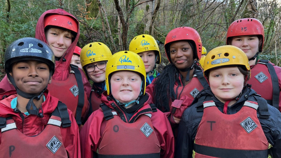 Pupils from Nunnery Wood High School in Worcester. All are smiling at the camera, wearing wet weather clothing, life-jackets and protective helmets.