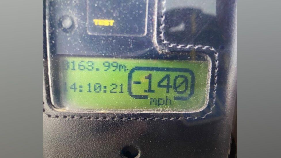 A green speedometer screen reading showing 140mph in a black case.