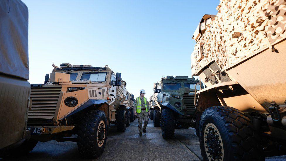 Two lines of army vehicles with man in high-vis walking between them.