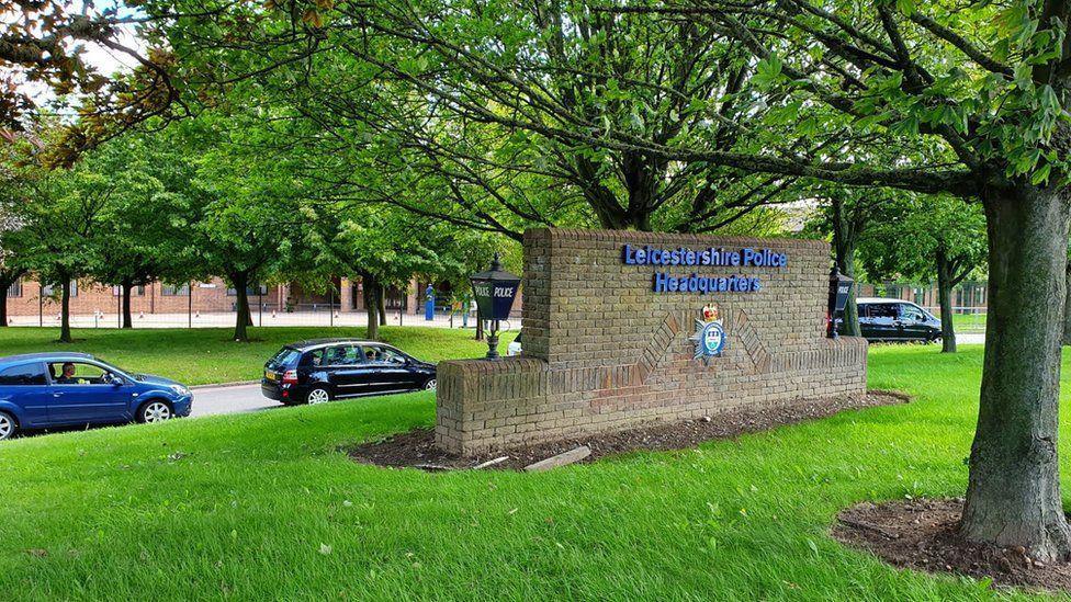 A photograph outside of Leicestershire Police Headquarters showing a wall with the force's name on and cars parked in the background