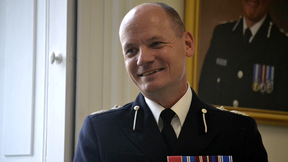 Alex Murray standing in a room with a portrait of a senior police officer hanging in the background