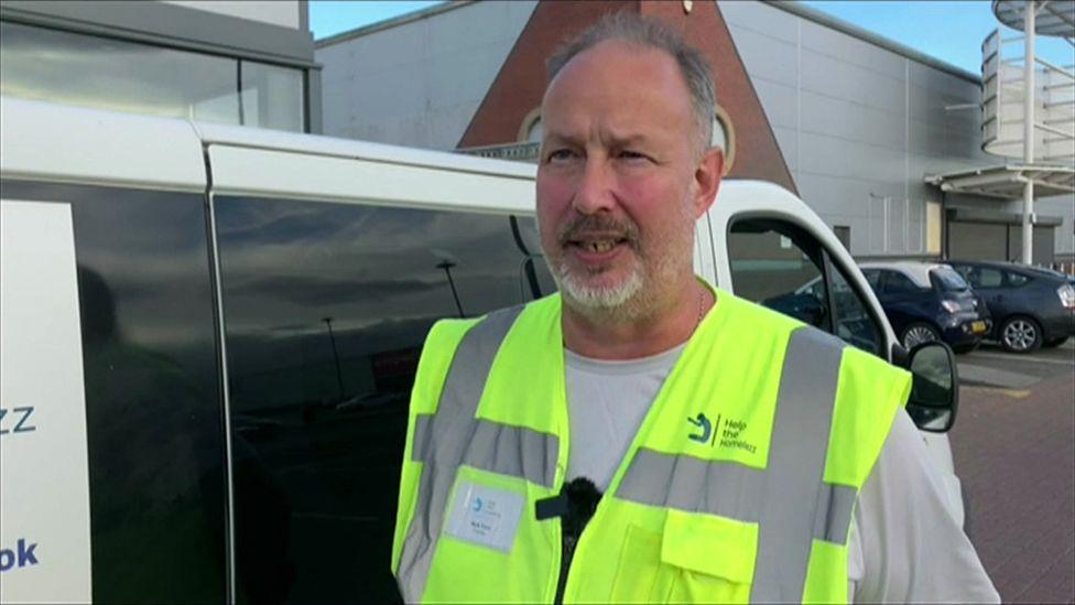 Mark Penn being interviewed wearing a white T-Shirt and a Hi-Vis jacket with a Help the Homelezz logo on it