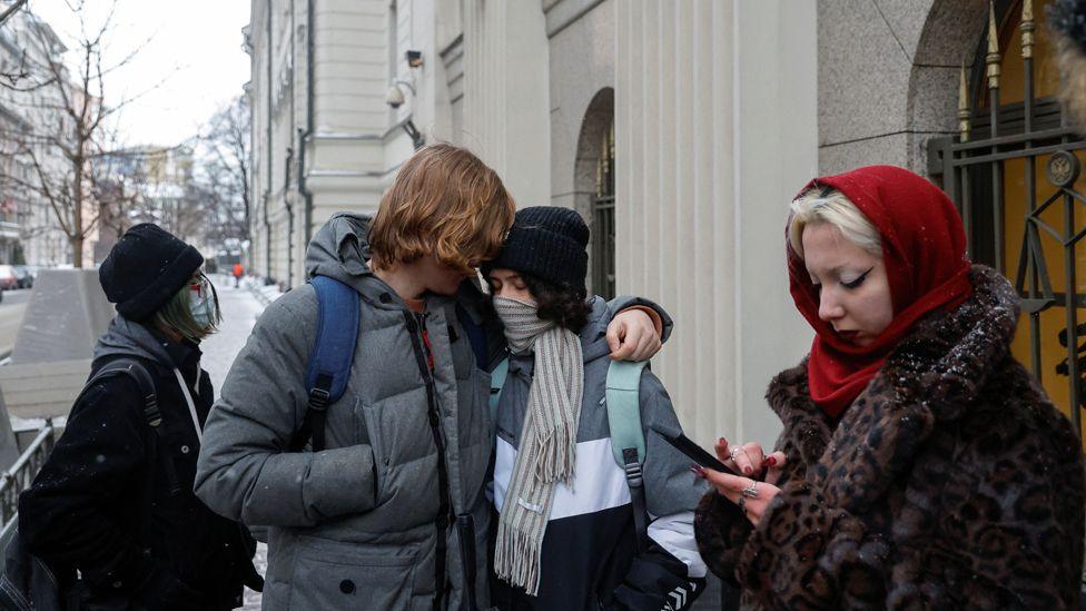 Ada with her arm around another young person, a few other people stand nearby outside the Supreme Court in Moscow