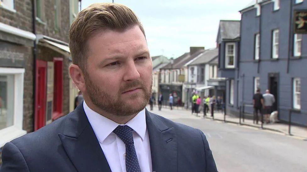 Senedd member Sam Kurtz stands in a street wearing a suit